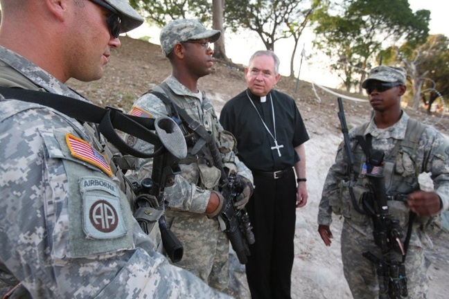At the huge refugee camp at a former golf course at Petionville Club, San Antonio Archbishop Jose Gomez talks with members of the U.S. Armed Forces. The archbishop was part of a delegation from the U.S. bishops conference who visited Haiti in early March. Catholic Relief Services is helping run the tent city at the former golf course.