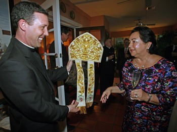 Father Richard Vigoa, priest secretary to Archbishop Thomas Wenski, explains to Maria Cristina Diaz of the Cuban Association of the Order of Malta how the precious miter is embroidered with the coat of arms of Archbishop Wenski.