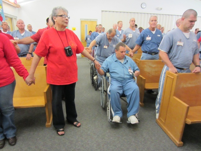 A volunteer with St. Louis Parish's "Rejoice in the Lord" prison ministry holds hands with inmates while praying the Our Father.