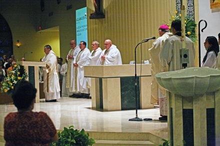 Deacon Edgardo Farias proclaims the Gospel as Father Jorge Presmanes, Father Marcelo Solarzano, Father Resituto Perez, Father Alberto Rodriguez, St. Dominic's pastor, and Archbishop Thomas Wenski listen. The new altar, podium and baptismal font are visible in this photo.
