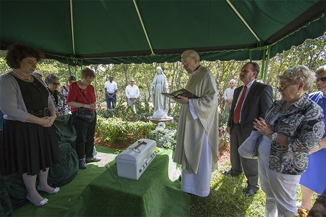Father Dominick O'Dwyer says the final prayers over the casket of Baby Gabriel before his burial in the baby section of Our Lady Queen of Heaven Cemetery in North Lauderdale. At left is Mary Ross Agosta, archdiocesan director of communications, and at right is Det. Jim Jaggers of the Fort Lauderdale Police Dept.