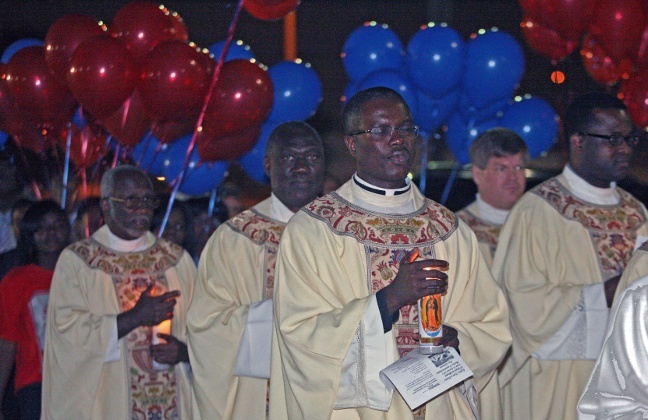 Priests and those attending the Mass walk in a candlelight procession to the courtyard where the candles were placed under a cross and balloons were released.