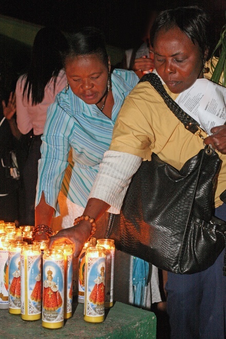 Two women place candles beside the cross in Notre Dame d'Haiti's courtyard.