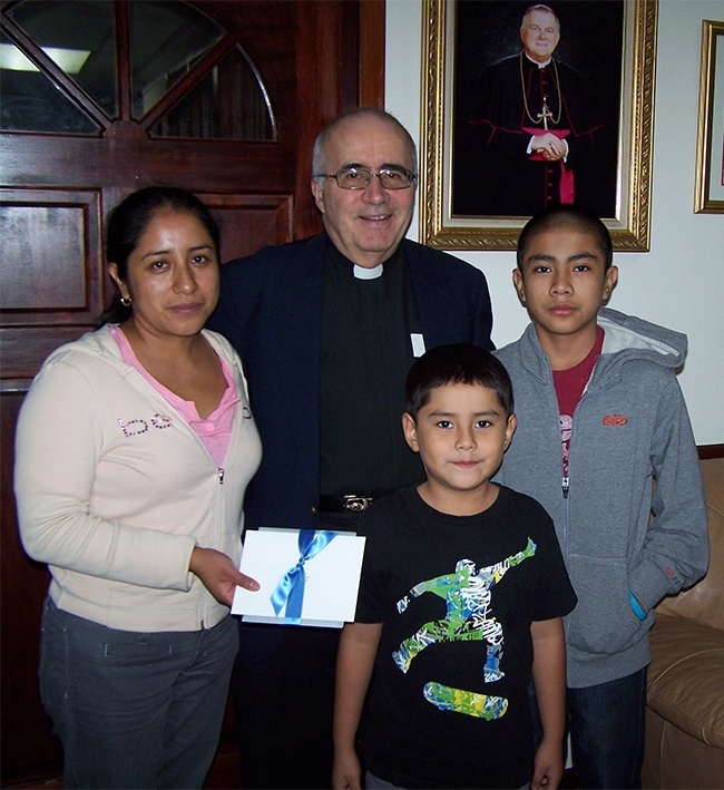 Jesuit Father Eduardo Alvarez, pastor of Gesu Church in Miami, hands a 0 gift certificate from Archbishop Thomas Wenski to Aura Herrera and her children, Marco, 7, and Roger, 11.