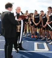 Father Kris Bartos, left, assistant principal for Christian Formation, and Father Brendan Dalton, supervising principal of Archbishop Edward McCarthy High School, prepare to bless the track with holy water.