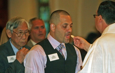 Jose Santiago, a candidate from St. Edward Church in Pembroke Pines, is accompanied by his sponsor, Trevor Chong, as  he receives his first Communion from Father Carlos Vega, pastor of St. Bernard Church in Sunrise.
