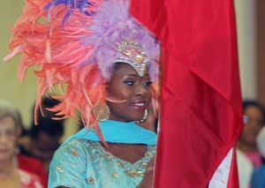 Shea McMayo, whose parents were born in Trinidad and Tobago, carries the flag into church while wearing a carnival head piece.