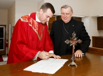 As Miami Archbishop Thomas Wenski looks on, Father David Toups signs church documents following the Rite of Installation of Rector on Sept. 21 at St. Vincent de Paul Regional Seminary in Boynton Beach.