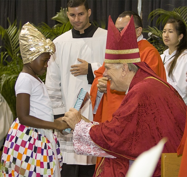 Archbishop Thomas Wenski receives an offertory gift from a Haitian girl: a religious education book.