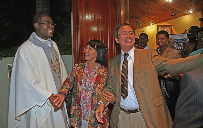 Dr. Gilbert Leung takes a photo as his wife, Theresa Leung, shakes hands with Father Jude after his farewell Mass.