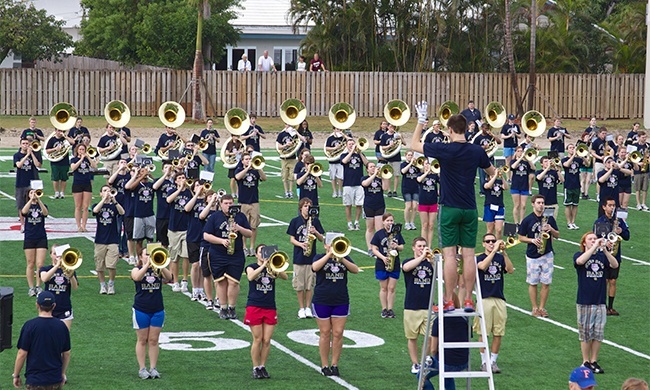 The marching band for Notre Dame's Fighting Irish rehearse their performance of "God bless America" as people peek over their backyard fences to watch. About 100 people also watched from the stands.