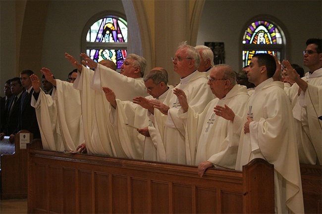 Priests extend their hands toward the Oil of Chrism during the blessing.