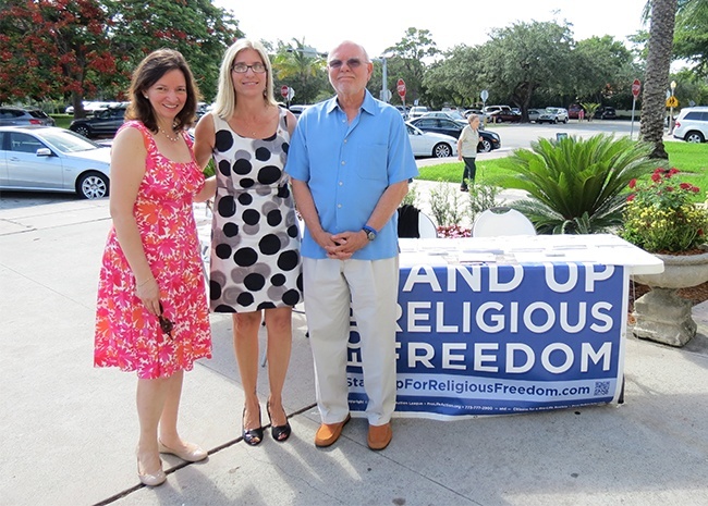 Cristina Sousa, left, Jena Getchell, center, and Felipe Vizcarrondo, right, show their support for the Fortnight for Freedom while standing outside Little Flower Church. They are  members of the Public Square Discipleship, a ministry set up by Little Flower's pastor, Father Michael Davis, to foster prayer and action for religious freedom.