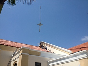 Workers guide a crane as it lowers the cross onto the roof of Notre Dame d'Haiti's new church.