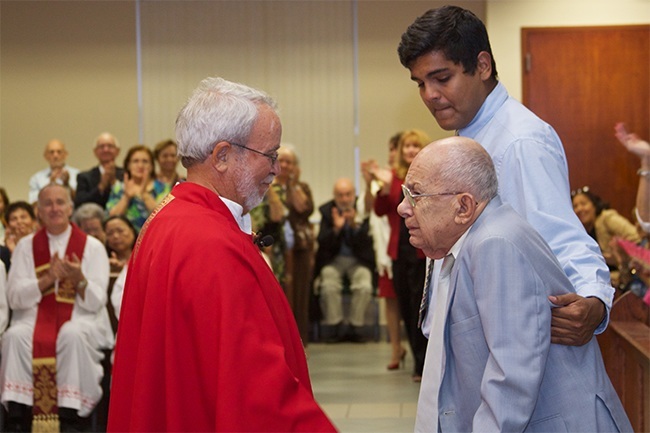 Father Fernando Compaired, founding pastor of Mother of Our Redeemer Parish, embraces Jose Luis Toby Sanchez, one of the founding members of the church during the offertory.