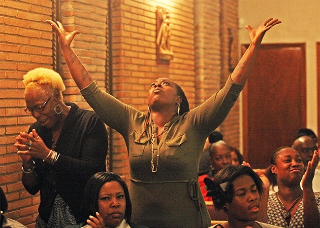 Dominique Wesby reacts to Father Anthony Bozeman's words during the annual black Catholic revival. Tammy Wesby, her mother, prays beside her.