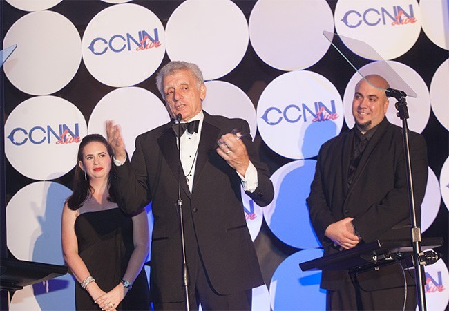 Salvatore Cannella addresses the audience after receiving an award as founder of CCNN. Looking on are Christina Hidalgo, journalism teacher, and Omar Delgado, CCNN live moderator and technology curriculum coordinator.