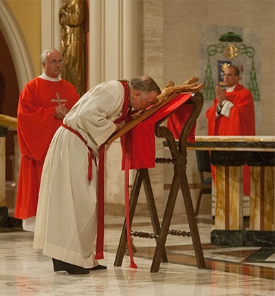 A shoeless Archbishop Thomas Wenski kisses the cross.