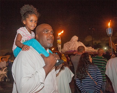 David Louis, one of the cantors who sang the Gospel account of the passion of Jesus, carries his niece, Heaven Goycohcha, 3, on his shoulders during the procession that followed the service.