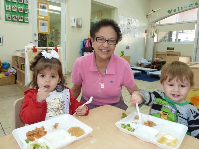 Clara Gesni, maestra de cuidado infantil en el Centro Mater hace 27 años, se retrata entre sus alumnos Leah LLanes y Angelo Falero durante la hora de almuerzo.